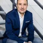 Christian Gottschling sitzt in blauem Sakko und Jeans entspannt auf den Stufen einer Außentreppe und blickt in die Kamera