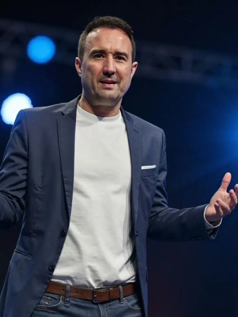 Christian Gottschling im blauen Sakko spricht auf einer Bühne mit blauen Scheinwerfern und erklärt mit offenen Händen